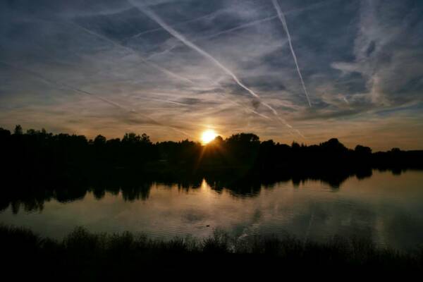 Contrails in the evening sky above a lake